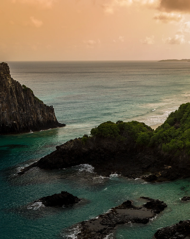 A calm image of the sky at sunset over the ocean, with jagged cliffs and forested land in the foreground. SÃO TOMÉ and PRÍNCIPE journey with Aurisé World.
